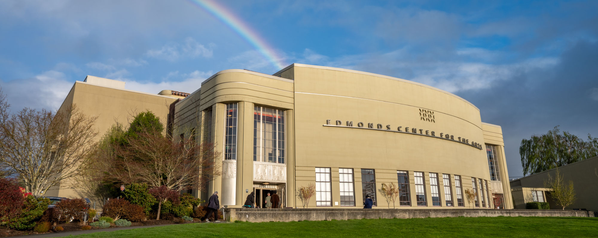 the edmonds center for the arts building shines in the late day sun, as a rainbow appears overhead amidst a blue sky